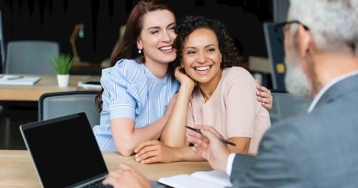 Two women smiling and embracing at a meeting.