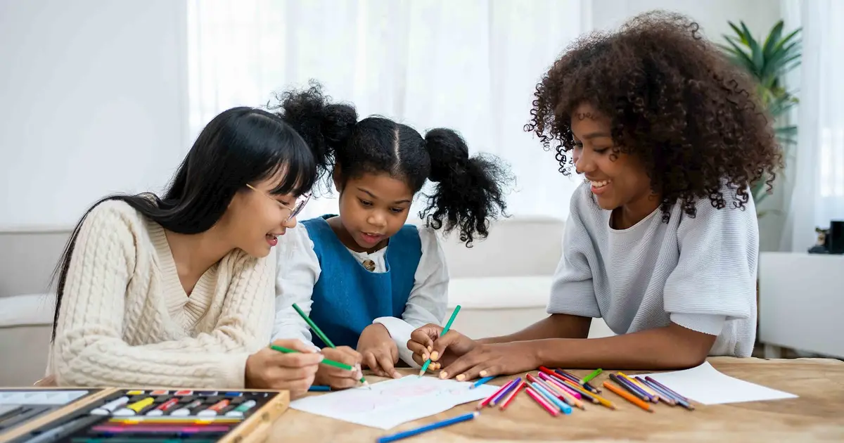 Three young girls drawing and coloring together, fostering creativity and friendship.