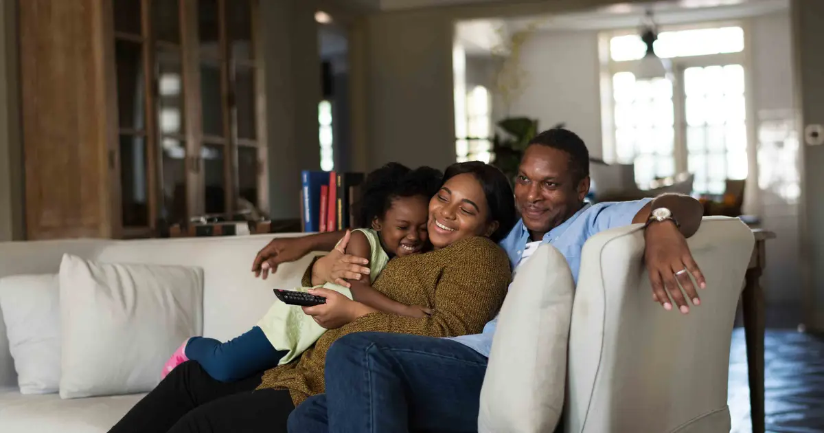 Happy family cuddles on sofa, smiling while watching TV together.