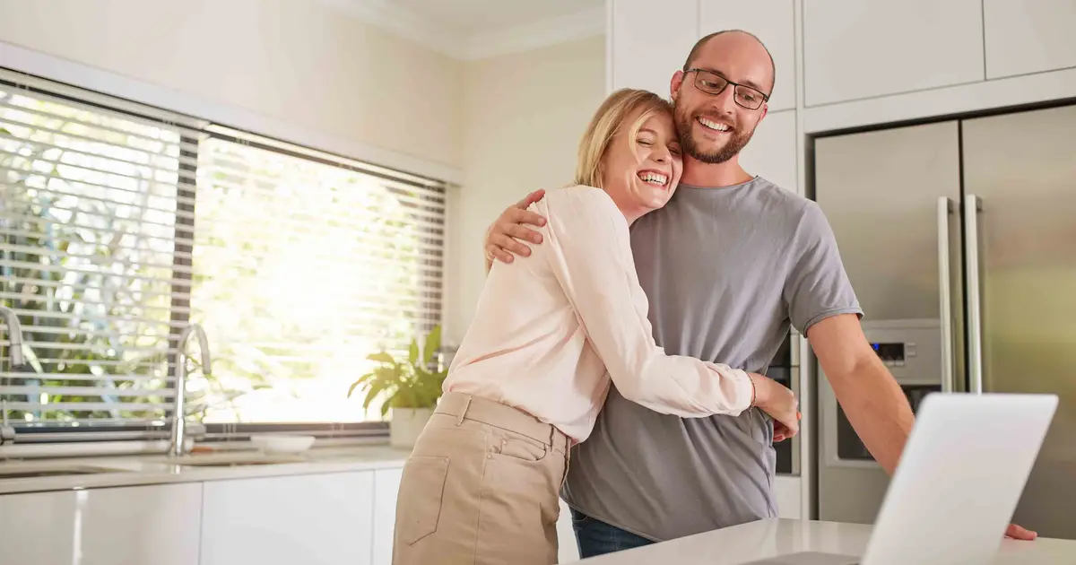 Smiling couple in kitchen looking at laptop, planning short-term rental.