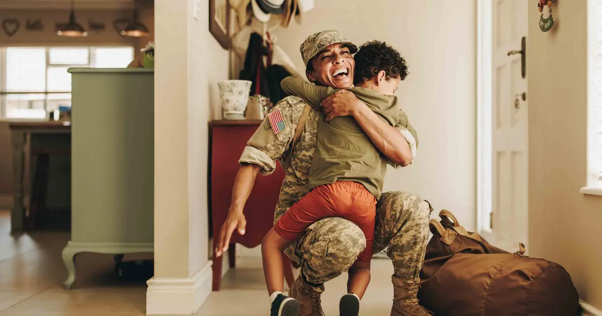 Military service member joyfully embraces child during emotional homecoming moment.