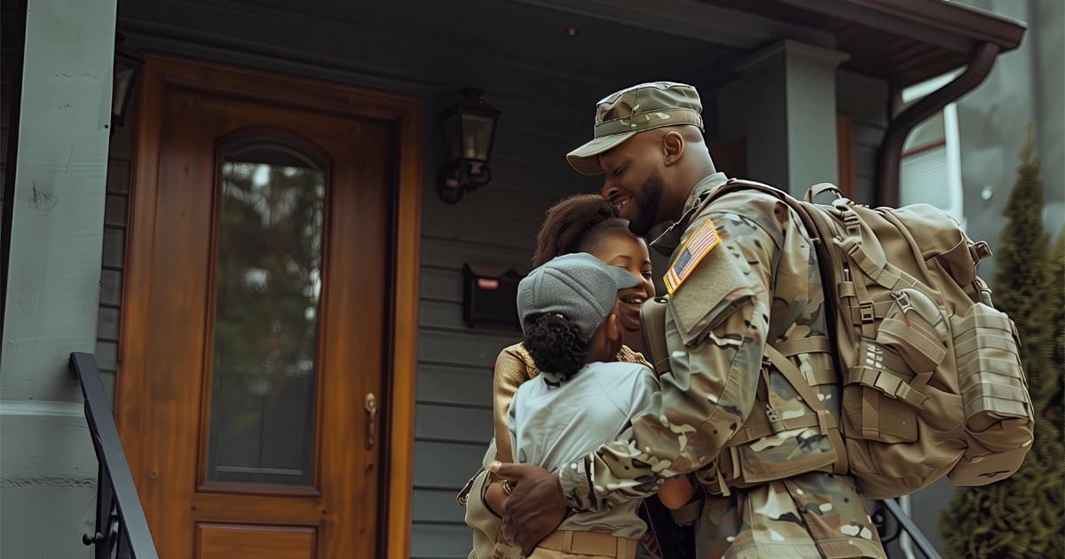 Service member reunites with family on porch in emotional homecoming embrace.