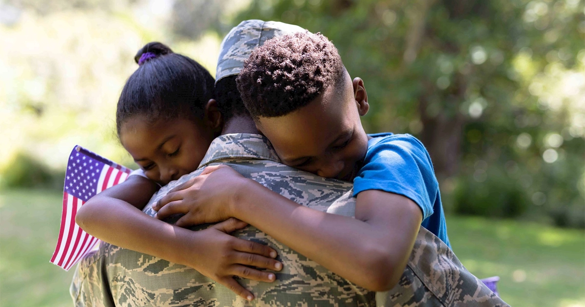 Military parent in uniform embraces two children in emotional outdoor reunion.