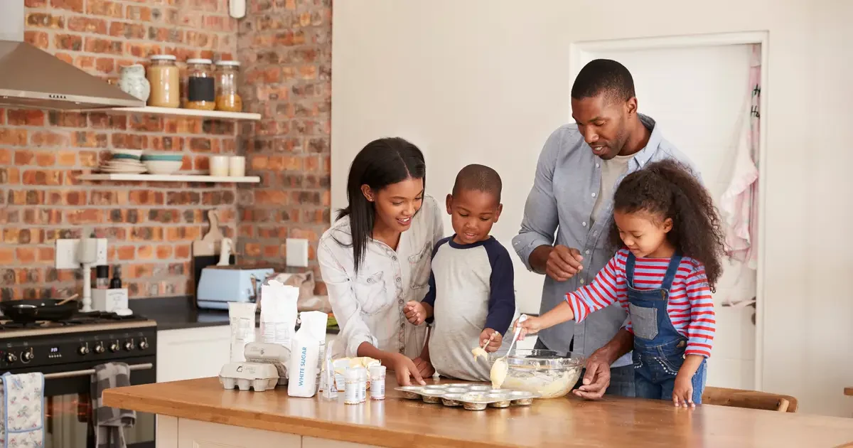 Family of four bakes muffins together in a bright, modern kitchen.