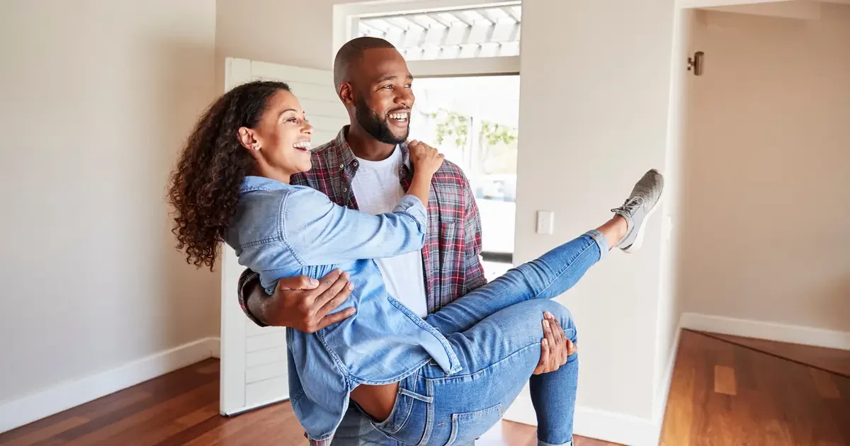 Man carrying woman in new home, both smiling